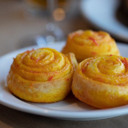A close-up of golden, spiral-shaped pastries with a glossy finish, placed on a light-colored plate.