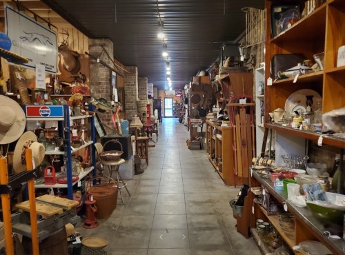 A narrow aisle in an antique shop filled with various vintage items and decor on both sides.