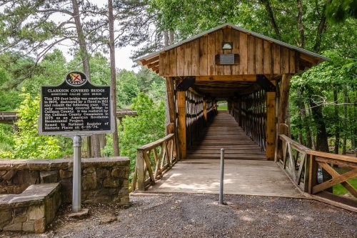 A wooden covered bridge surrounded by trees, with a historical marker at the entrance.