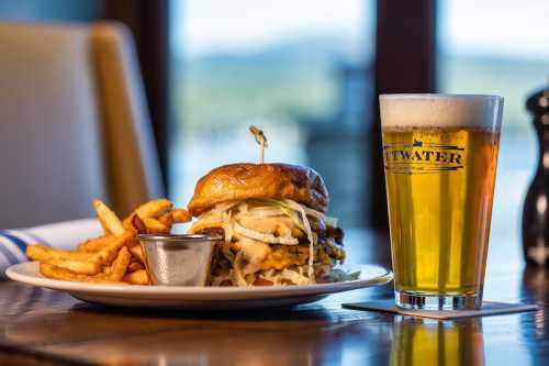 A delicious burger with fries and a pint of beer on a table, with a scenic view in the background.