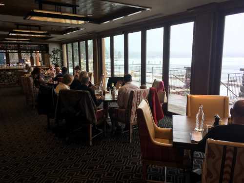 A cozy restaurant interior with large windows, diners at tables, and a view of a foggy outdoor landscape.