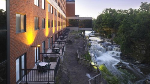 A riverside hotel with balconies overlooking a waterfall, surrounded by lush greenery at dusk.