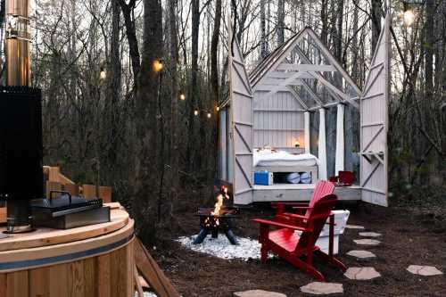 Cozy outdoor cabin with an open design, fire pit, and red chairs, surrounded by trees and string lights.