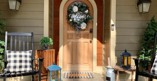 A welcoming front porch with a wooden door, wreath, rocking chairs, and decorative lanterns.