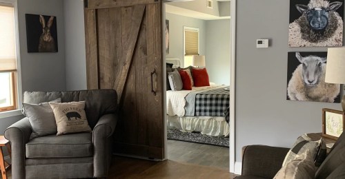 Cozy living room with a gray sofa, wooden sliding door, and a glimpse of a bedroom featuring sheep-themed decor.