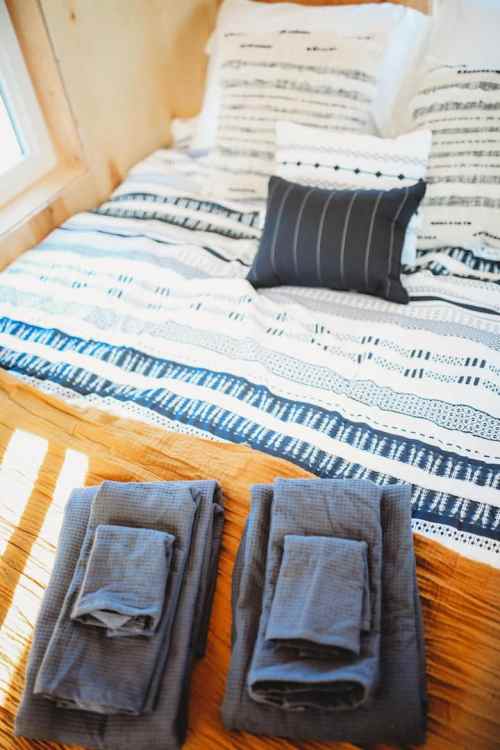 A neatly made bed with patterned pillows and a striped blanket, flanked by two folded towels on the floor.