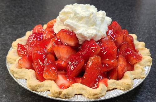 A delicious strawberry pie topped with whipped cream, featuring a golden crust and glistening red strawberries.