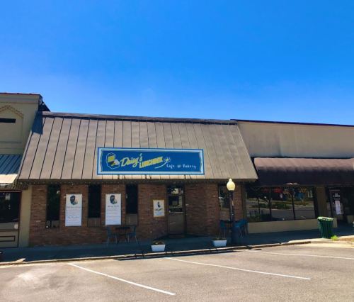 A cafe and bakery with a blue sign, located in a brick building under a clear blue sky. Outdoor seating visible.