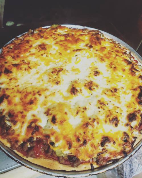 A freshly baked pizza topped with melted cheese, ground meat, and vegetables, golden and bubbling.