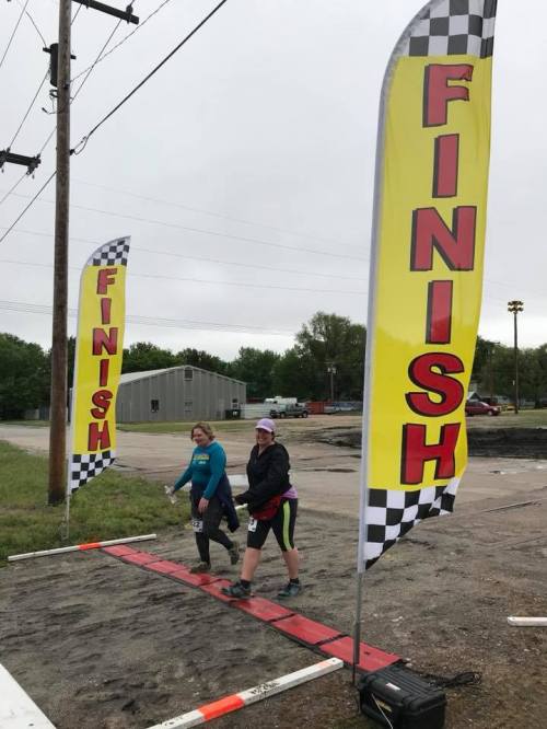 Two women crossing a finish line marked by large "FINISH" banners on a cloudy day.
