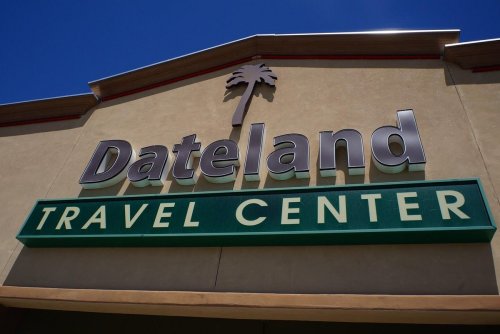 Sign for Dateland Travel Center featuring a palm tree logo against a clear blue sky.