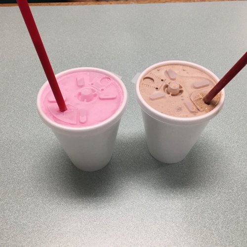 Two cups with red straws: one pink drink and one brown drink, placed on a light green table.