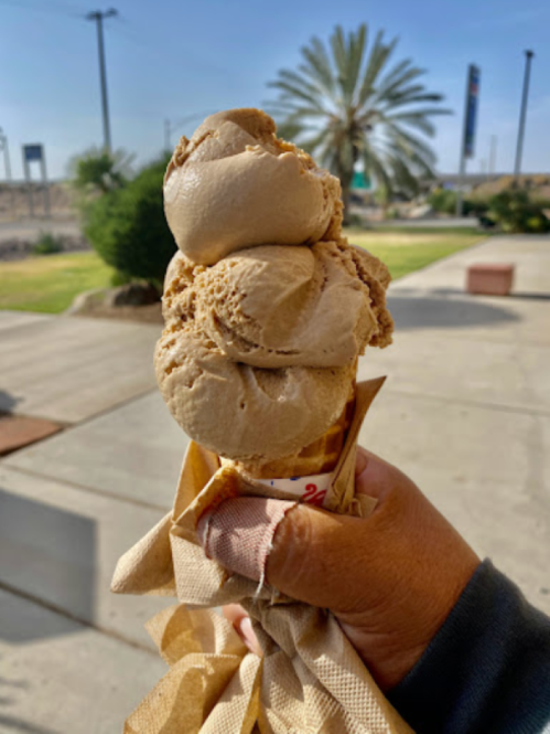 A hand holding a triple scoop ice cream cone with a palm tree and sunny sky in the background.