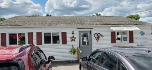A white building with red shutters, a star decoration, and an "OPEN" sign, surrounded by parked cars under a cloudy sky.
