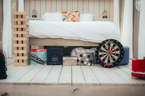 A cozy bedroom with a bed, games like Jenga, Battleship, and a dartboard displayed on a wooden floor.