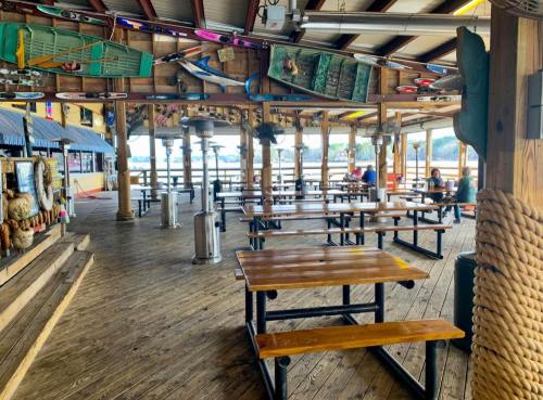 A spacious outdoor dining area with wooden tables, a rustic decor, and views of the water in the background.