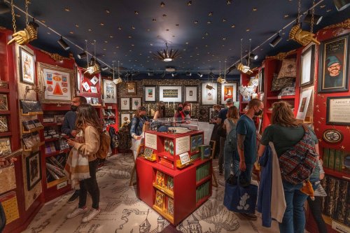 A cozy bookstore interior filled with colorful displays, art, and people browsing among books and decorations.