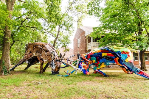 Colorful, large-scale sculptures of animals made from recycled materials, set in a green outdoor area near a historic building.