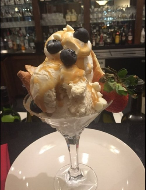 A delicious ice cream sundae topped with blueberries, caramel sauce, and a strawberry, served in a glass.