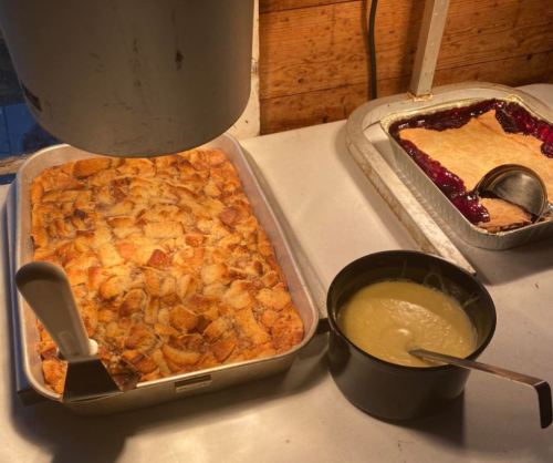 A tray of baked dessert next to a bowl of sauce and a dish of berry filling on a countertop.