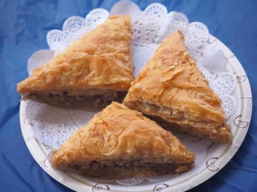 Three triangular pieces of baklava on a decorative paper doily, arranged on a plate.
