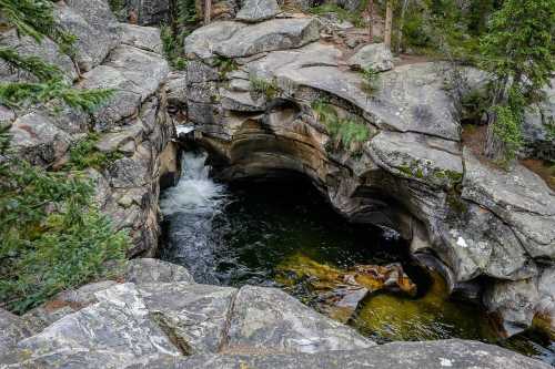 A serene rocky landscape featuring a small waterfall flowing into a dark pool surrounded by lush greenery.