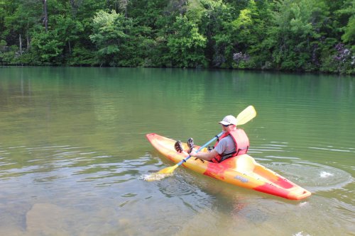 A person kayaking on a calm lake surrounded by lush green trees.