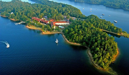 Aerial view of a lush green island with a resort, surrounded by calm blue waters and boats in the distance.