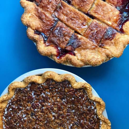 Two delicious pies on a blue background: a lattice-topped fruit pie and a pecan pie dusted with powdered sugar.