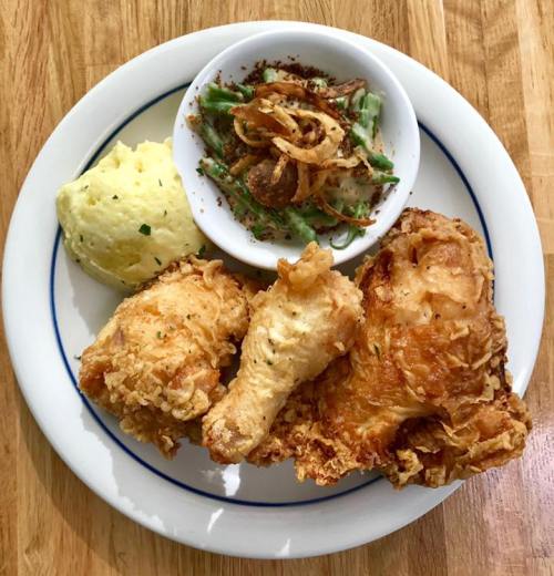 A plate of fried chicken with mashed potatoes, green beans topped with crispy onions, and a side of gravy.