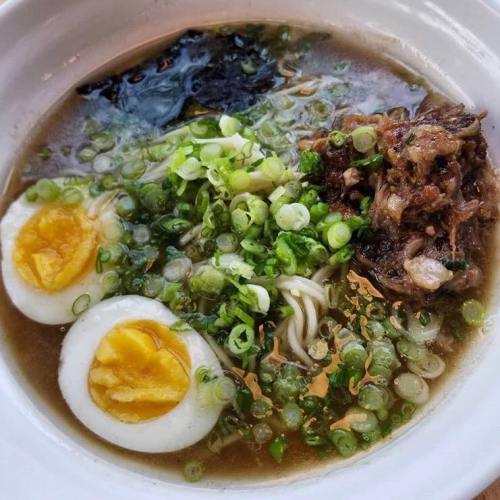 A bowl of ramen with soft-boiled eggs, green onions, seaweed, and tender meat in a savory broth.