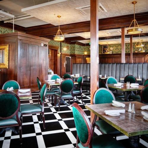 Elegant restaurant interior featuring dark wood paneling, green velvet chairs, and a black-and-white checkered floor.