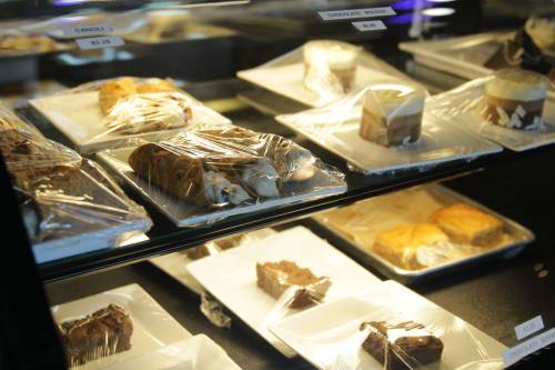 Display case filled with various desserts, including cakes and pastries, all covered in plastic wrap.