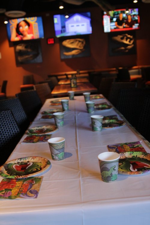 A long table set for a party, decorated with themed plates and cups, in a lively restaurant with TVs in the background.