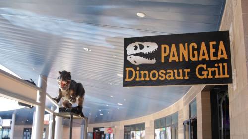 Sign for "Pangaea Dinosaur Grill" with a dinosaur statue displayed above it in a modern indoor setting.
