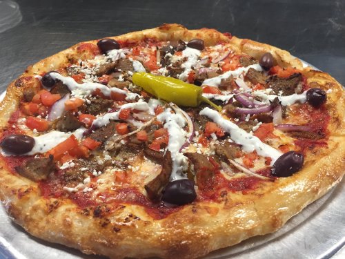 A delicious pizza topped with meat, tomatoes, olives, onions, feta cheese, and a pepper, drizzled with sauce.