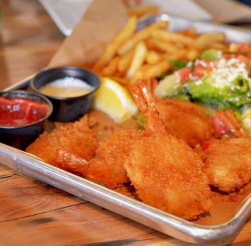 A platter with crispy fried shrimp, French fries, a lemon wedge, and dipping sauces on a wooden table.