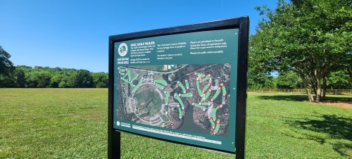 A sign displaying a map of a disc golf course, surrounded by green grass and trees in the background.