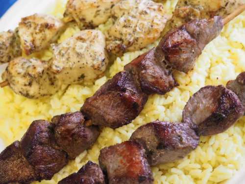 Grilled chicken and beef skewers served over a bed of yellow rice on a white plate.
