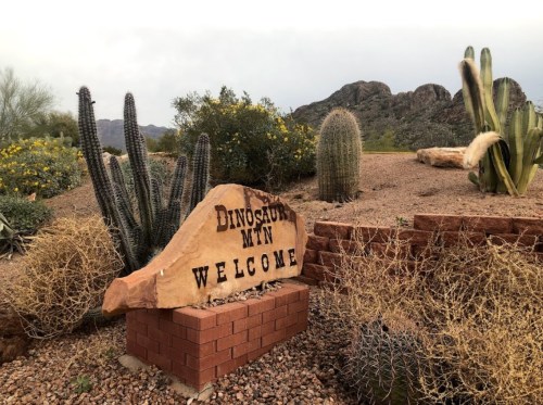A welcome sign for Dinosaur Mountain surrounded by desert plants and rocky terrain.