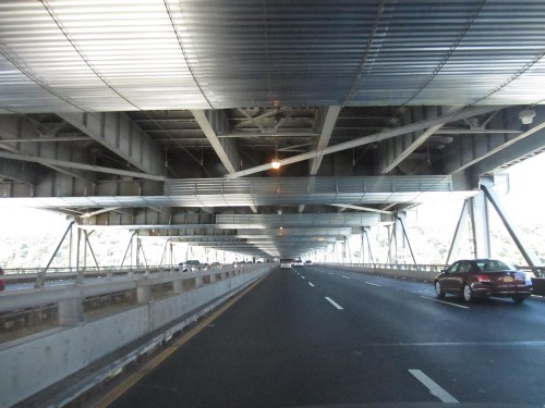 View from underneath a bridge, showcasing metal supports and vehicles on the road above.