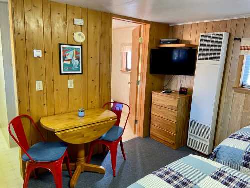 Cozy room with wooden walls, a small table and chairs, a dresser, and a wall-mounted TV.