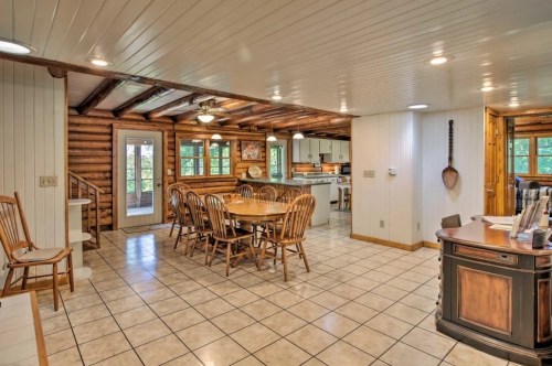 Cozy log cabin interior featuring a dining area, kitchen, and wooden decor with tiled flooring and natural light.