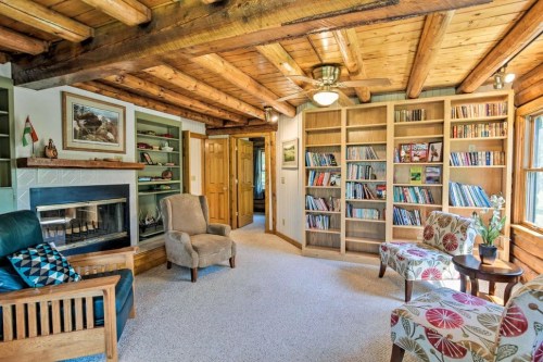 Cozy living room with wooden beams, a fireplace, bookshelves, and comfortable seating. Bright and inviting atmosphere.