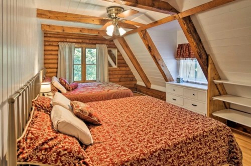 Cozy attic bedroom with two beds, wooden beams, and a large window letting in natural light.