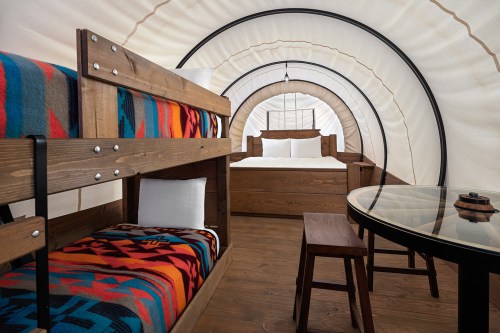 Cozy interior of a glamping tent featuring a bunk bed, a double bed, and a wooden table with chairs.