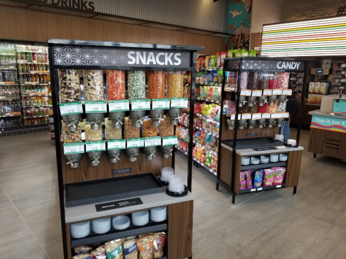 A snack and candy station with various dispensers filled with nuts, dried fruits, and sweets in a store.