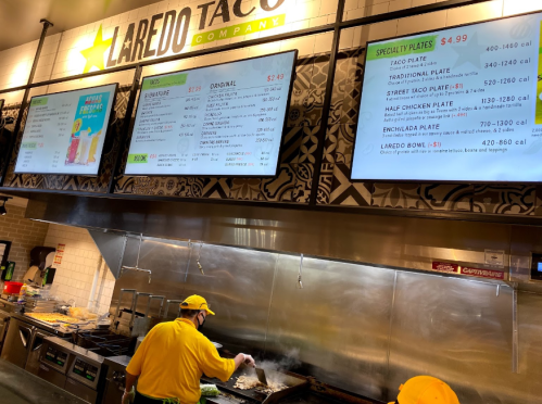 A restaurant menu displays various taco and plate options, with staff cooking in the kitchen below.