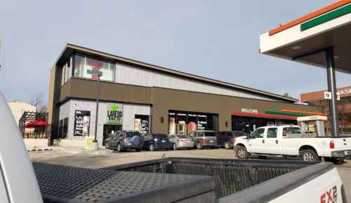 A modern building with a Latino Taco restaurant and a convenience store, surrounded by parked cars.