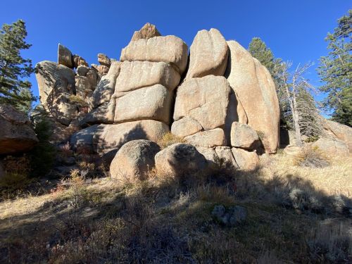 Large, rugged rock formations surrounded by sparse vegetation and trees under a clear blue sky.
